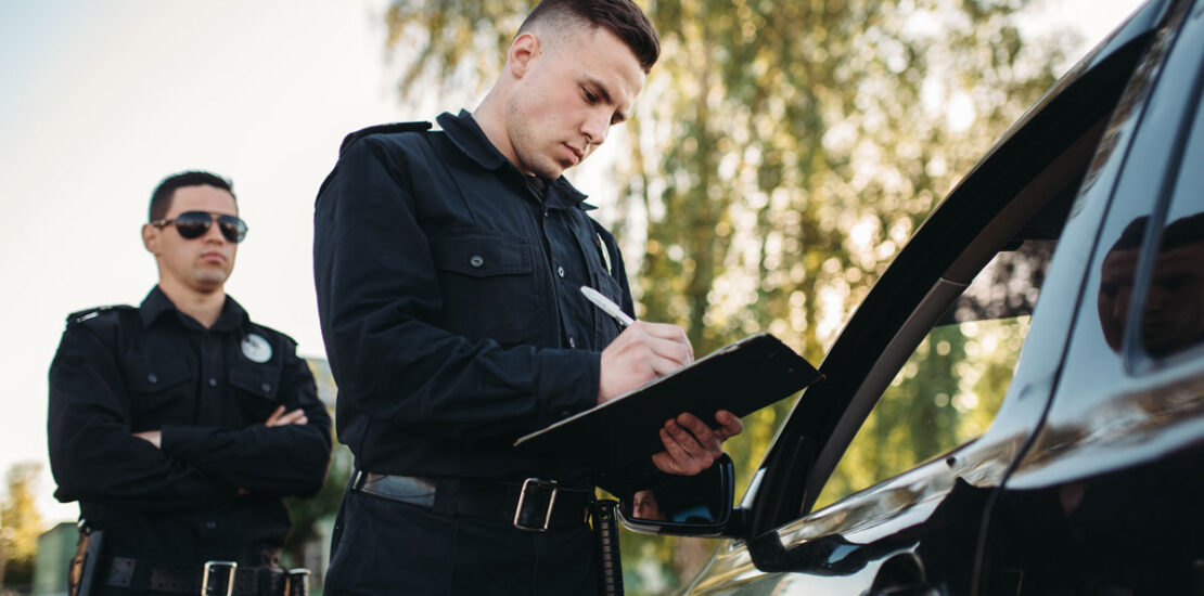 Two male police officers standing by a pulled-over car, suggesting the need for a criminal lawyer.
