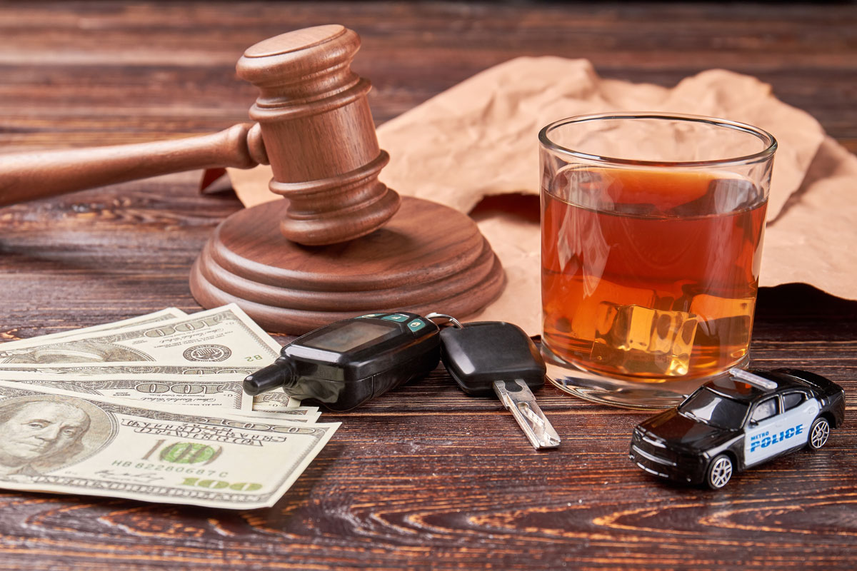 Argent, clés de voiture, une voiture de police-jouet et un verre d'alcool sur une table avec le maillet du juge, représentant les risques de la conduite avec facultés affaiblies.