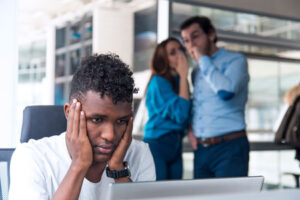 A man being harassed at work by two coworkers, symbolizing the need for a workplace harassment lawyer.