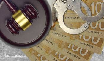 Money, handcuffs, and a judge's gavel on a desk, implying the need for a criminal lawyer.