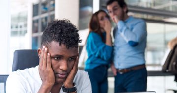 A man being harassed at work by two coworkers, symbolizing the need for a workplace harassment lawyer.